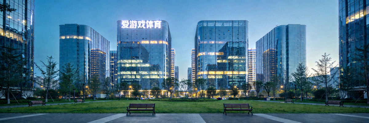 爱游戏体育大厦外景图：一座现代化的玻璃幕墙写字楼，楼顶有爱游戏体育的发光标识，前方是绿化广场