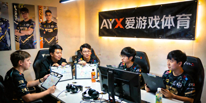 DOTA2战队五位选手在训练室中围坐讨论战术，墙壁上装饰着AYX爱游戏体育的横幅